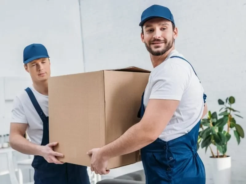 Two men in overalls carrying a box, working together in a professional setting.